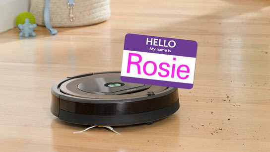 A robot vacuum on a dirty floor with a name tag saying “Hello, my name is Rosie”.