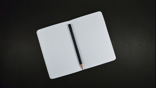 A pencil resting in the folded margin of a notebook opened on a blank page.