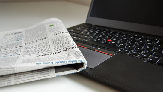 A folded newspaper lays on top of a laptop computer with a switched-off display.