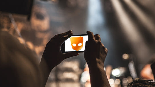 A pair of hands holding up a smartphone with the Grindr app icon on the screen.