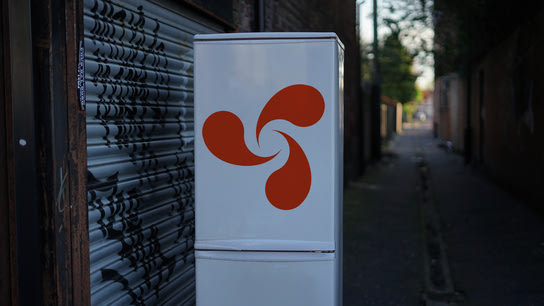A refrigerator with the Opera Unite logo on the front door. The frige is sitting outside in a back alley.