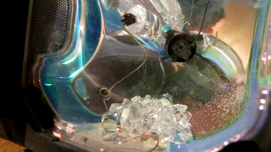 A blown projector lamp bulb with bits of glass debris and dust inside it.