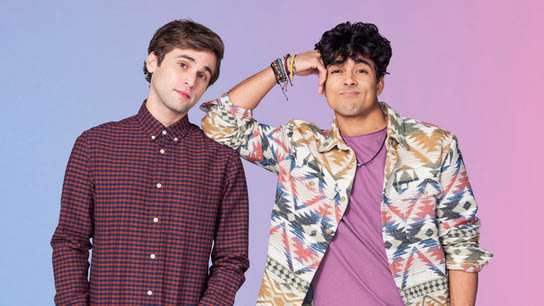 Two handsome guys are standing shoulder to shoulder. One is wearing business casual and looks expectantly at the camera. The other is wearing a Hawaii-style shirt and smirks at the camera.