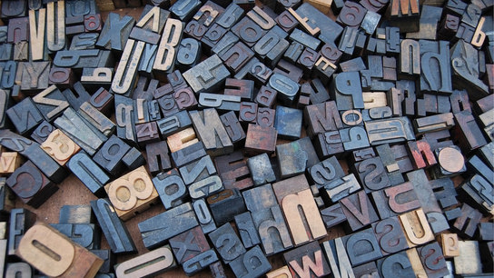 A scattered set of wooden typesetting letters and symbols.